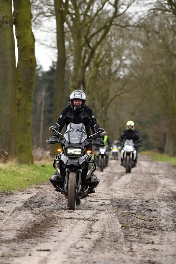 Lachende motorrijder op een BMW GS voorop een groep op een modderig bospad